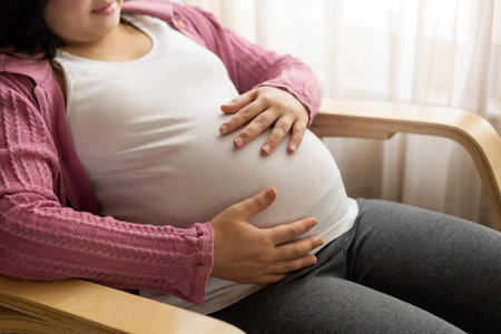 Pregnant woman feeling happy at home while taking care of her child. The young expecting mother...