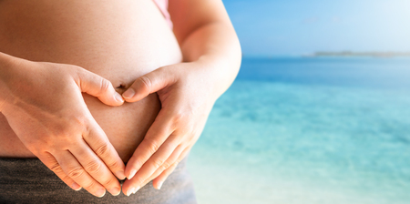 Pregnant woman feeling happy with new life at the beach in summer travel while take care of her child. The young expecting mother holding baby in pregnant belly. Maternity and woman pregnancy concept.の写真素材
