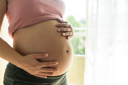 Pregnant woman feeling happy at home while taking care of her child. The young expecting mother holding baby in pregnant belly. Maternity prenatal care and woman pregnancy concept.の写真素材