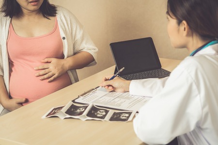 Happy pregnant woman visit gynecologist doctor at hospital or medical clinic for pregnancy consultant. Doctor examine pregnant belly for baby and mother healthcare check up. Gynecology concept.の写真素材