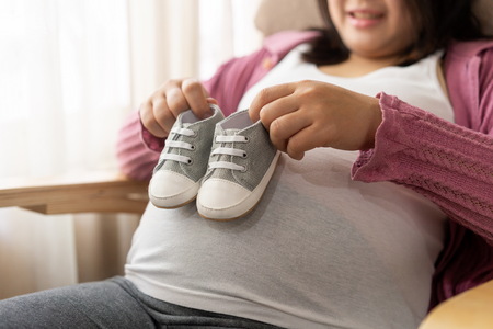 Pregnant woman feeling happy at home while taking care of her child. The young expecting mother holding baby in pregnant belly. Maternity prenatal care and woman pregnancy concept.の写真素材