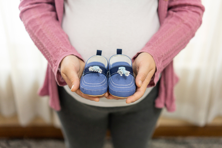 Pregnant woman feeling happy at home while taking care of her child. The young expecting mother holding baby in pregnant belly. Maternity prenatal care and woman pregnancy concept.の写真素材
