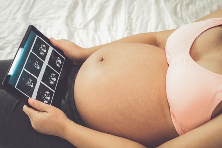 Pregnant woman feeling happy at home while taking care of her child. The young expecting mother holding baby in pregnant belly. Maternity prenatal care and woman pregnancy concept.の写真素材