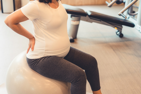 Active pregnant woman exercise in fitness center at yoga room. The young expecting mother holding baby in pregnant belly. Maternity prenatal care and woman pregnancy concept.の写真素材