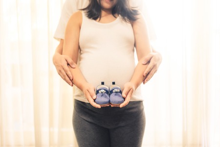 Pregnant couple of husband and wife feels love and relax at home. Young expecting woman holds baby in pregnant belly. Father take care of pregnant mother. Concept of maternity and pregnancy care.の写真素材