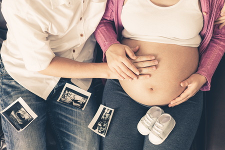 Pregnant couple of husband and wife feels love and relax at home. Young expecting woman holds baby in pregnant belly. Father take care of pregnant mother. Concept of maternity and pregnancy care.の写真素材