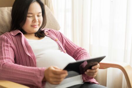 Pregnant woman feeling happy at home while taking care of her child. The young expecting mother holding baby in pregnant belly. Maternity prenatal care and woman pregnancy concept.の写真素材