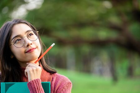 Young creative student girl thinking or planning future education while holding pencil in hand. Creativity idea and learning concept.の写真素材