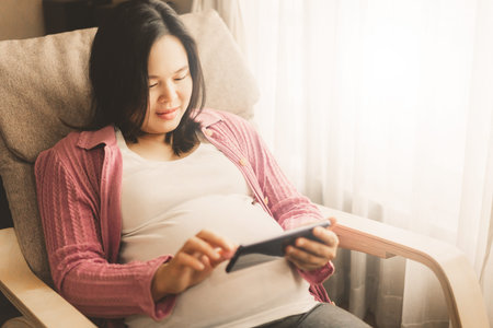 Pregnant woman feeling happy at home while taking care of her child. The young expecting mother...