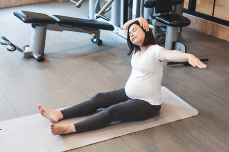 Active pregnant woman exercise in fitness center at yoga room. The young expecting mother holding baby in pregnant belly. Maternity prenatal care and woman pregnancy concept.の写真素材