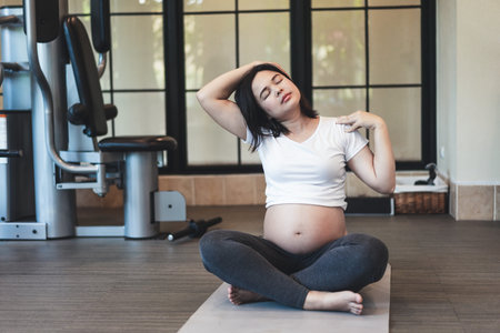 Active pregnant woman exercise in fitness center at yoga room. The young expecting mother holding baby in pregnant belly. Maternity prenatal care and woman pregnancy concept.の写真素材