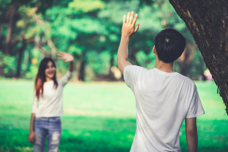 Young people, man and woman greeting or saying goodbye by waving hands in the park.