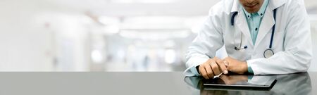 Male doctor sitting at table with tablet computer in hospital office. Medical healthcare staff and doctor service.の写真素材