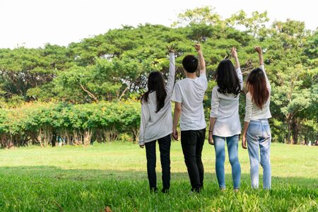Young happy students of men and women raising hands celebrating and showing teamwork in the park of school or university. Charity, volunteer and unity concept.の写真素材