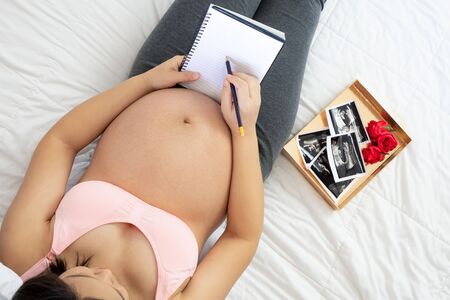 Pregnant woman feeling happy at home while taking care of her child. The young expecting mother holding baby in pregnant belly. Maternity prenatal care and woman pregnancy concept.の写真素材