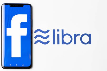 Bangkok, Thailand - July 2, 2019: Phone with Facebook logo on screen is placed on paper with Libra logo. Facebook reported to utilize new cryptocurrency called Libra expected to be used on Facebook.のeditorial素材