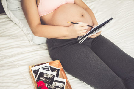 Pregnant woman feeling happy at home while taking care of her child. The young expecting mother...