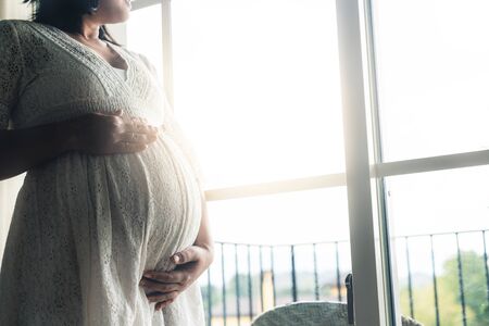 Pregnant woman feeling happy at home while taking care of her child. The young expecting mother holding baby in pregnant belly. Maternity prenatal care and woman pregnancy concept.の写真素材