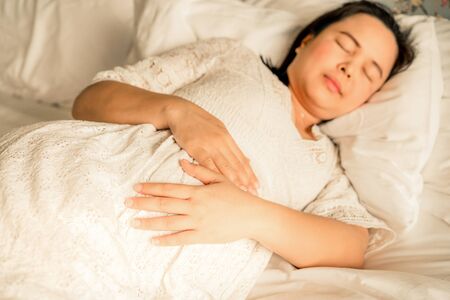 Pregnant woman feeling happy at home while taking care of her child. The young expecting mother holding baby in pregnant belly. Maternity prenatal care and woman pregnancy concept.の写真素材