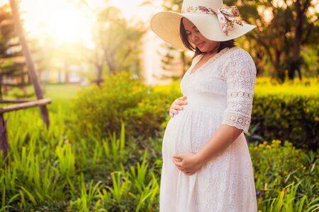 Pregnant woman feeling happy with new life at garden home while take care of her child. The young expecting mother holding baby in pregnant belly. Maternity prenatal care and woman pregnancy concept.の写真素材
