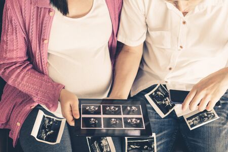 Pregnant couple of husband and wife feels love and relax at home. Young expecting woman holds baby in pregnant belly. Father take care of pregnant mother. Concept of maternity and pregnancy care.の写真素材