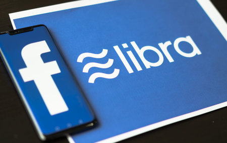 Bangkok, Thailand - July 2, 2019: Phone with Facebook logo on screen is placed on paper with Libra logo. Facebook reported to utilize new cryptocurrency called Libra expected to be used on Facebook.のeditorial素材