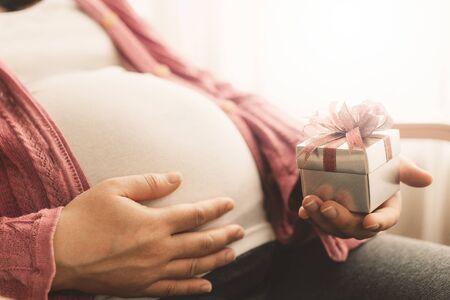 Pregnant woman feeling happy at home while taking care of her child. The young expecting mother holding baby in pregnant belly. Maternity prenatal care and woman pregnancy concept.の写真素材