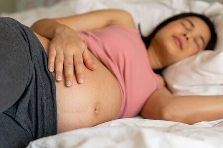 Pregnant woman feeling happy at home while taking care of her child. The young expecting mother holding baby in pregnant belly. Maternity prenatal care and woman pregnancy concept.の写真素材