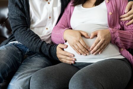 Pregnant couple of husband and wife feels love and relax at home. Young expecting woman holds baby in pregnant belly. Father take care of pregnant mother. Concept of maternity and pregnancy care.の写真素材