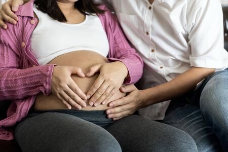 Pregnant couple of husband and wife feels love and relax at home. Young expecting woman holds baby in pregnant belly. Father take care of pregnant mother. Concept of maternity and pregnancy care.の写真素材