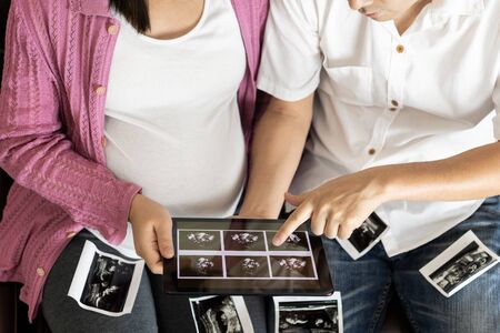Pregnant couple of husband and wife feels love and relax at home. Young expecting woman holds baby in pregnant belly. Father take care of pregnant mother. Concept of maternity and pregnancy care.の写真素材