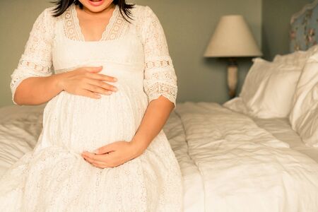 Pregnant woman feeling happy at home while taking care of her child. The young expecting mother holding baby in pregnant belly. Maternity prenatal care and woman pregnancy concept.の写真素材