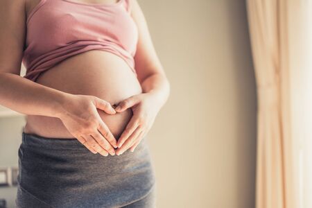 Pregnant woman feeling happy at home while taking care of her child. The young expecting mother holding baby in pregnant belly. Maternity prenatal care and woman pregnancy concept.の写真素材