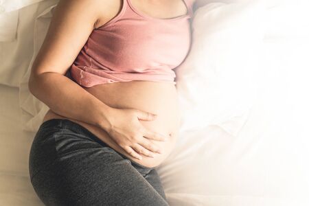 Pregnant woman feeling happy at home while taking care of her child. The young expecting mother holding baby in pregnant belly. Maternity prenatal care and woman pregnancy concept.の写真素材