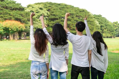 Young happy students of men and women raising hands celebrating and showing teamwork in the park of school or university. Charity, volunteer and unity concept.の写真素材