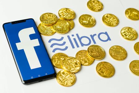 Bangkok, Thailand - July 2, 2019: Phone with Facebook logo on screen is placed on paper with Libra logo. Facebook reported to utilize new cryptocurrency called Libra expected to be used on Facebook.のeditorial素材