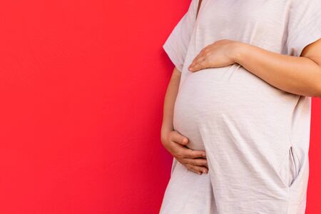 Pregnant woman feeling happy at home while taking care of her child. The young expecting mother holding baby in pregnant belly. Maternity prenatal care and woman pregnancy concept.の写真素材