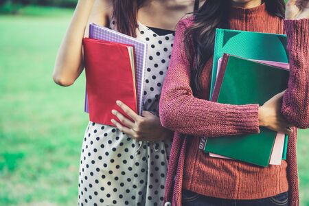 Young woman students friends hold books in their hand while standing in college park. Education concept.の写真素材