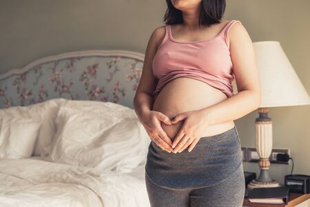 Pregnant woman feeling happy at home while taking care of her child. The young expecting mother holding baby in pregnant belly. Maternity prenatal care and woman pregnancy concept.の写真素材