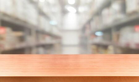 Wood table in warehouse storage blur background with empty copy space on the table for product display mockup. Hardware goods distribution and industrial logistics concept.の写真素材