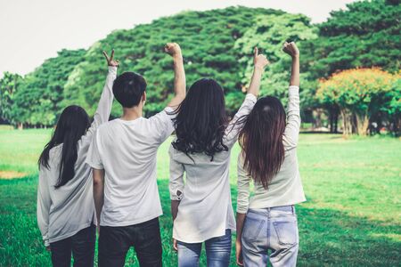 Young happy students of men and women raising hands celebrating and showing teamwork in the park of school or university. Charity, volunteer and unity concept.の写真素材