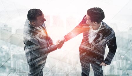 Double exposure image of business people handshake on city office building in background showing partnership success of business deal. Concept of corporate teamwork, trust partner and work agreement.の写真素材