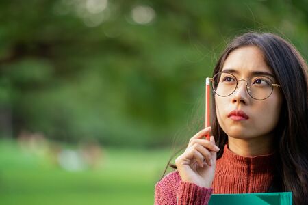 Young creative student girl thinking or planning future education while holding pencil in hand. Creativity idea and learning concept.の写真素材