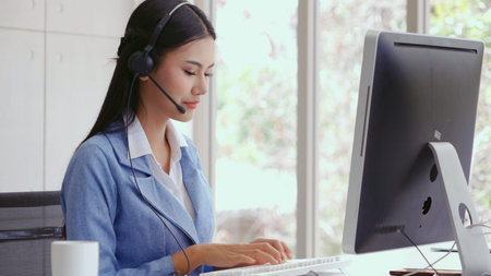Customer support agent or call center with headset works on desktop computer while supporting the...