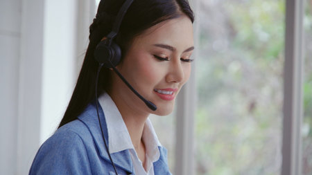 Customer support agent or call center with headset works on desktop computer while supporting the...