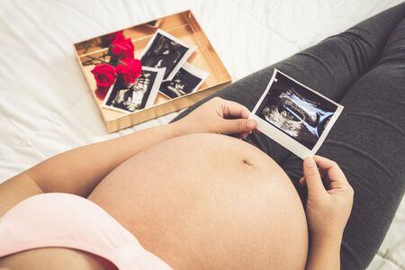 Pregnant woman feeling happy at home while taking care of her child. The young expecting mother holding baby in pregnant belly. Maternity prenatal care and woman pregnancy concept.の写真素材