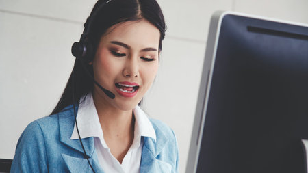 Customer support agent or call center with headset works on desktop computer while supporting the...