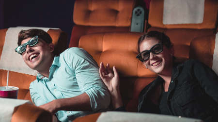 Man and woman in the cinema watching a movie with 3D glasses. with interest looking at the screen, exciting and eating popcornの写真素材