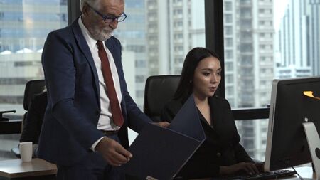 Senior manager gives advice to young woman worker in modern office. Leadership and training concept.の写真素材