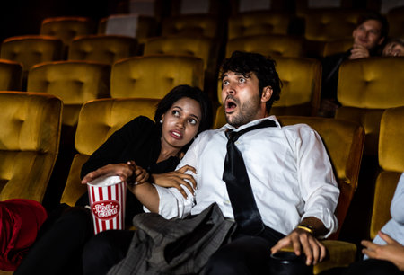 Shocked couple men and woman watch a horror movie at the cinemaの写真素材